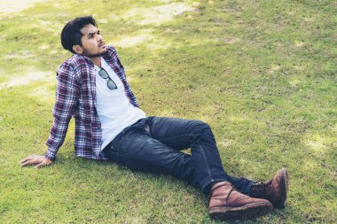 Yeşil çim düşünme üzerinde oturan genç adam