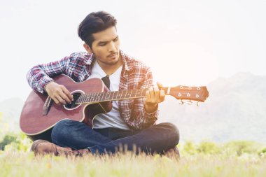 Yakışıklı adam yeşil çimenlerin üzerinde gitar çalmak