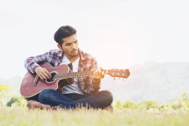 Yakışıklı adam yeşil çimenlerin üzerinde gitar çalmak