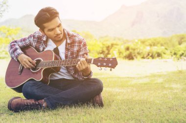 Yakışıklı adam yeşil çimenlerin üzerinde gitar çalmak