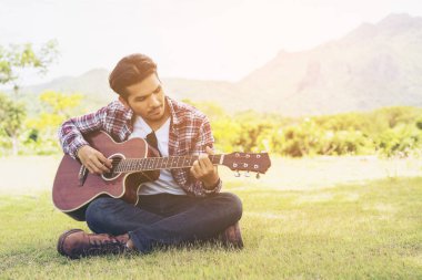 Yakışıklı adam yeşil çimenlerin üzerinde gitar çalmak