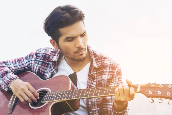 Handsome man playing guitar on green grass