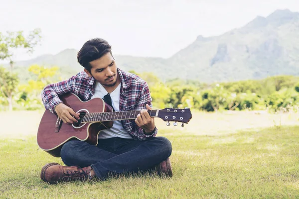 Handsome man playing guitar on green grass