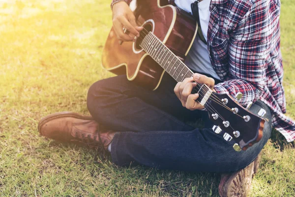 Mão de homem tocando guitarra, sentado na grama verde — Fotografia de Stock