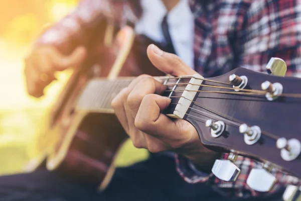 Man 's hand playing guitar, sitting on green grass — Stock Photo, Image
