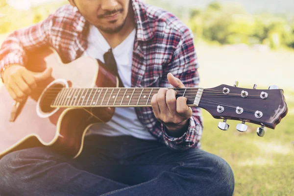 La mano del hombre tocando la guitarra, sentado en la hierba verde —  Fotos de Stock