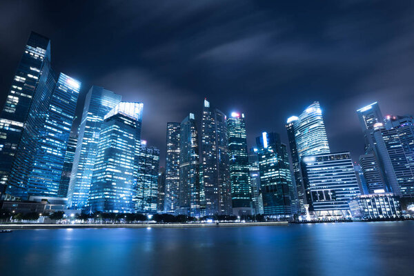 Modern city skyline at night with illuminated skyscrapers over water surface. Singapore central business district city skyline at marina bay. Modern architecture. Skyscrapers in Singapore downtown.