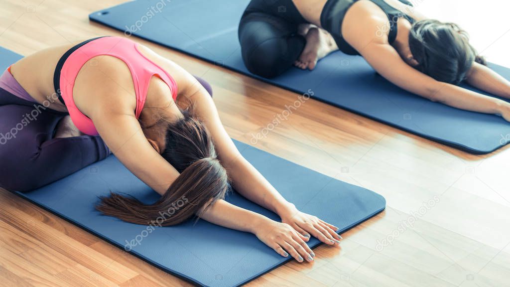 Women doing back stretching yoga in fitness gym