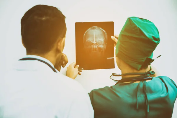 Врачи смотрят рентгеновские снимки головы пациента — стоковое фото