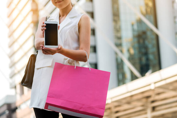 Woman with shopping bag showing phone screen.