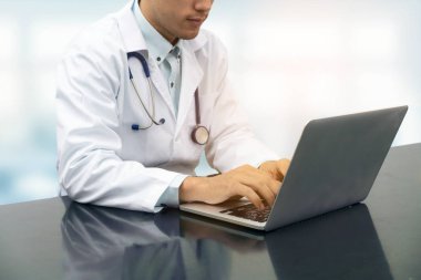 Dizüstü bilgisayar ile masa üzerinde çalışan doktor