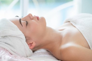Rahatlamış genç bir kadın masaj için spa yatağında yatıyor..