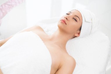 Rahatlamış genç bir kadın masaj için spa yatağında yatıyor..