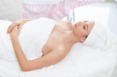 Rahatlamış genç bir kadın masaj için spa yatağında yatıyor..