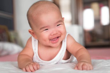 İlk kez gülümseyen şirin bir bebek emekliyor. Mutlu Asyalı bebek yatak odasında oynuyor..