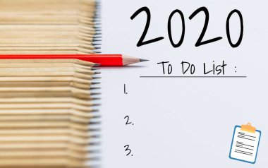 Yeni Yıl Hedefleri Listesi 2020 - Yeni yıl hedefleri ve kararları sıralaması hakkında el yazısıyla yazılmış bir not defteri ile iş yeri masası. Değişim ve kararlılık kavramı.