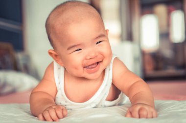 İlk kez gülümseyen şirin bir bebek emekliyor. Mutlu Asyalı bebek yatak odasında oynuyor..