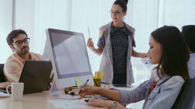 Kıdemli lider takım üyelerine tavsiye konuşması yapıyor. Modern ofisteki masada yaratıcı iş adamları buluşuyor. Çok kültürlü iş ekibi..
