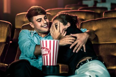 Bir çift beyaz sinemada gerilim filmi izler, kadın gözleri kapanır ve yüzünü ekrandan çevirir.