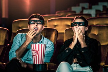 Sinemada üç boyutlu gözlüklü bir kadın ve erkek film izliyor. Ekrana bakar, heyecan verici ve patlamış mısır yer.