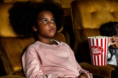 İki Afrikalı ve Asyalı çocuk sinemada eğleniyor ve film izlemekten zevk alıyor.