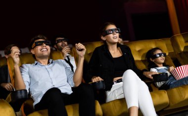 Bir grup insan, sinemada 3D gözlüklü bir film izliyor. Ekrana bakıyor, heyecan verici ve eğleniyor.