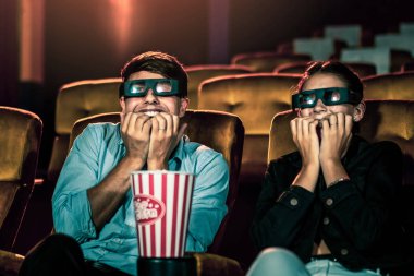 Sinemada üç boyutlu gözlüklü bir kadın ve erkek film izliyor. Ekrana bakar, heyecan verici ve patlamış mısır yer.