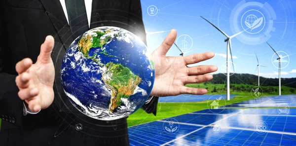 Concept of sustainability development by alternative energy. Man hand take care of planet earth with environmentally friendly wind turbine farm and green renewable energy in background.