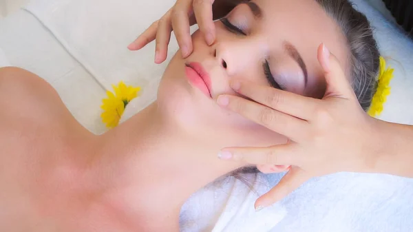 Relaxed woman lying on spa bed for facial and head massage spa treatment by massage therapist in a luxury spa resort. Wellness, stress relief and rejuvenation concept.