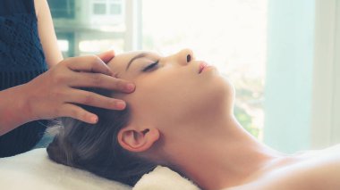 Lüks bir spa merkezinde masaj terapisti tarafından yüz masajı ve spa tedavisi için kaplıcaya uzanmış rahat bir kadın. Sağlık, stres atma ve gençleştirme kavramı.