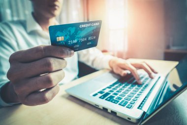 Genç adam, laptop bilgisayar başvurusu ya da web sitesinde online alışveriş yapmak için kredi kartı kullanıyor. E-ticaret ve online alışveriş kavramı.