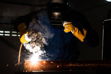 Fabrikada çelik kaynak makinesiyle çalışan metal kaynakçı güvenlik ekipmanı takıyor. El becerisi iş gücü kavramına göre metal imalatı ve inşaat bakım hizmeti.