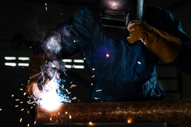 Fabrikada çelik kaynak makinesiyle çalışan metal kaynakçı güvenlik ekipmanı takıyor. El becerisi iş gücü kavramına göre metal imalatı ve inşaat bakım hizmeti.