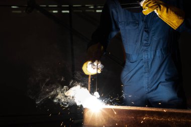Fabrikada çelik kaynak makinesiyle çalışan metal kaynakçı güvenlik ekipmanı takıyor. El becerisi iş gücü kavramına göre metal imalatı ve inşaat bakım hizmeti.