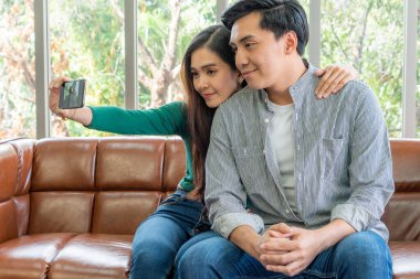 Mutlu Asyalı çift evdeki oturma odasında cep telefonuyla selfie çekmeyi sever..