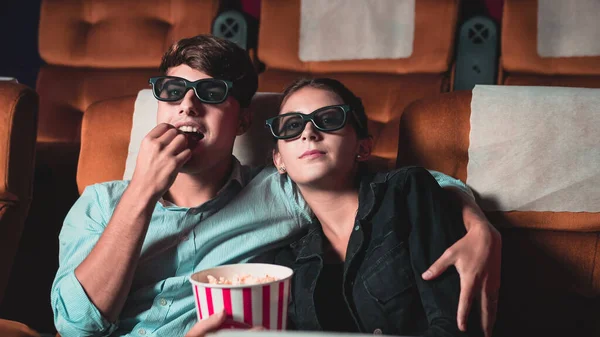 Man and woman in the cinema watching a movie with 3D glasses. with interest looking at the screen, exciting and eating popcorn