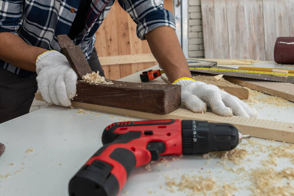 Carpenter working on wood craft at workshop to produce construction material or wooden furniture. The young Asian carpenter use professional tools for crafting. DIY maker and carpentry work concept.