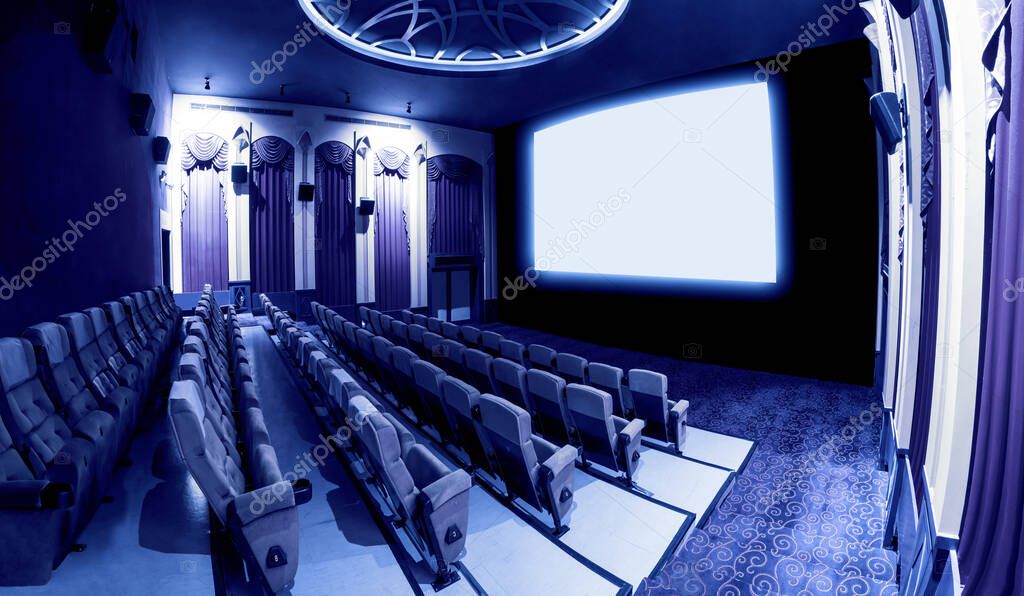 Cinema theater screen in front of seat rows in movie theater showing white screen projected from cinematograph. The cinema theater is decorated in classical style for luxury feeling of movie watching.