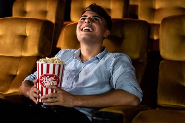 Genç bir adam sinemada film izlerken patlamış mısırla eğleniyor.