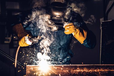 Fabrikada çelik kaynak makinesiyle çalışan metal kaynakçı güvenlik ekipmanı takıyor. El becerisi iş gücü kavramına göre metal imalatı ve inşaat bakım hizmeti.