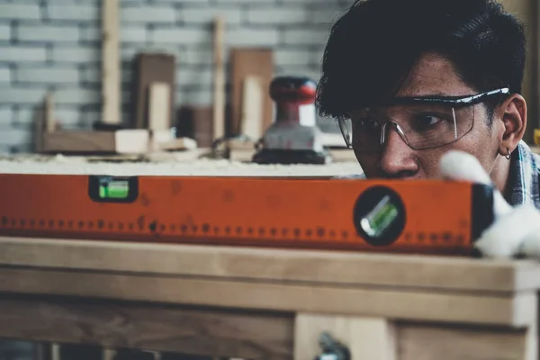 Carpenter working on wood craft at workshop to produce construction material or wooden furniture. The young Asian carpenter use professional tools for crafting. DIY maker and carpentry work concept.