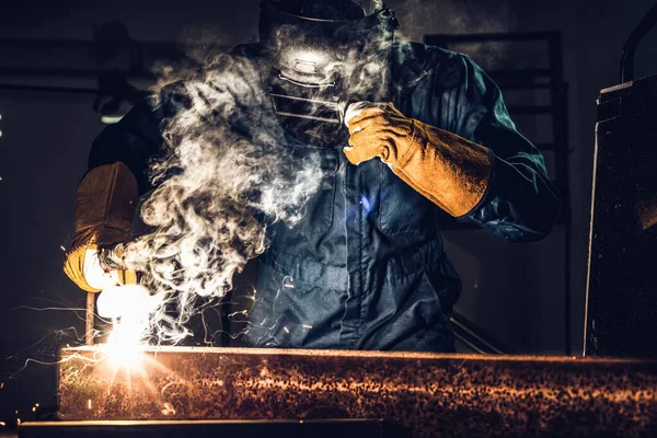 Metal welder working with arc welding machine to weld steel at factory while wearing safety equipment. Metalwork manufacturing and construction maintenance service by manual skill labor concept.