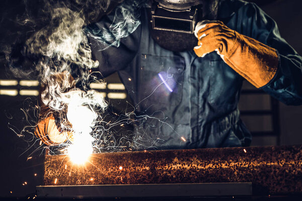 Metal welder working with arc welding machine to weld steel at factory while wearing safety equipment. Metalwork manufacturing and construction maintenance service by manual skill labor concept.