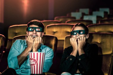 Sinemada üç boyutlu gözlüklü bir kadın ve erkek film izliyor. Ekrana bakar, heyecan verici ve patlamış mısır yer.