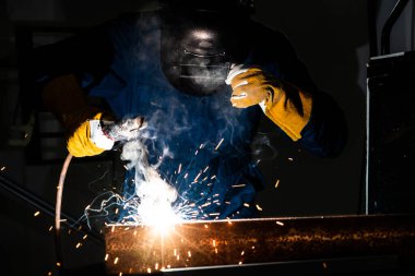 Fabrikada çelik kaynak makinesiyle çalışan metal kaynakçı güvenlik ekipmanı takıyor. El becerisi iş gücü kavramına göre metal imalatı ve inşaat bakım hizmeti.