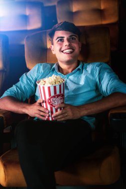 Genç bir adam sinemada film izlerken patlamış mısırla eğleniyor.