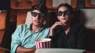 Sinemada üç boyutlu gözlüklü bir kadın ve erkek film izliyor. Ekrana bakar, heyecan verici ve patlamış mısır yer.