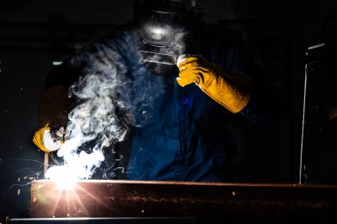 Fabrikada çelik kaynak makinesiyle çalışan metal kaynakçı güvenlik ekipmanı takıyor. El becerisi iş gücü kavramına göre metal imalatı ve inşaat bakım hizmeti.