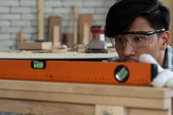 Carpenter working on wood craft at workshop to produce construction material or wooden furniture. The young Asian carpenter use professional tools for crafting. DIY maker and carpentry work concept.