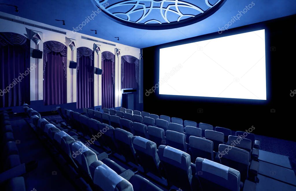 Cinema theater screen in front of seat rows in movie theater showing white screen projected from cinematograph. The cinema theater is decorated in classical style for luxury feeling of movie watching.